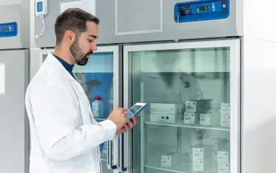 Physician recording information in front of fridge with vaccines